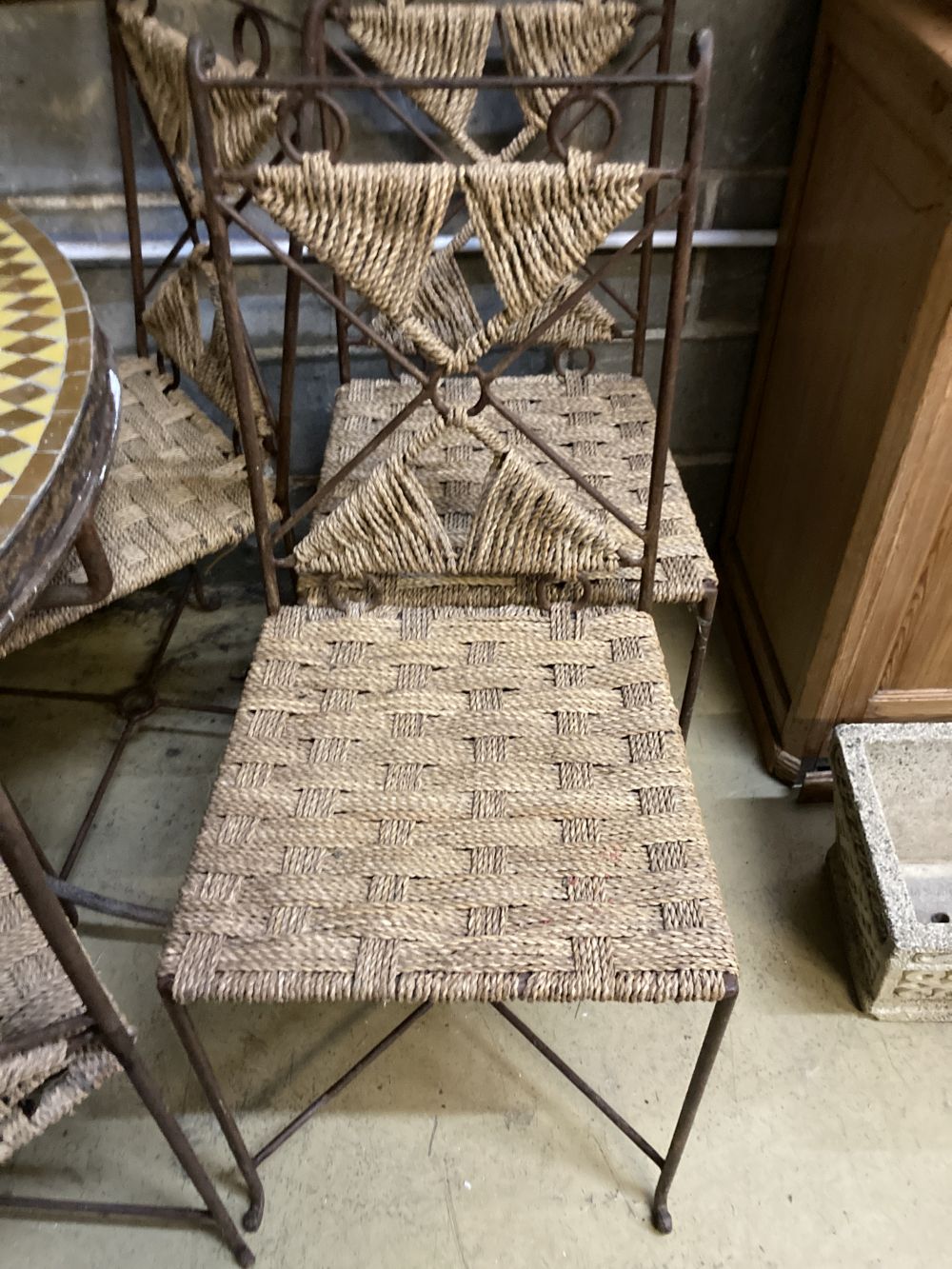 An iron framed circular tiled top table, a set of six iron framed chairs, with rope work seats and a wrought iron easel, table 128 diam